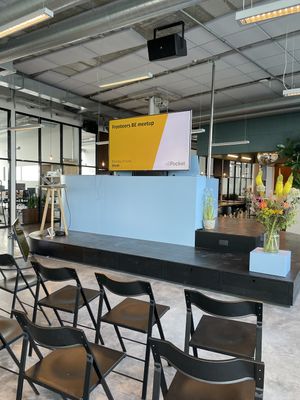 The still empty meetup space, with chairs set up to face the small stage and presenter screen. On the presenter screen a slide is visible introducting the Fronteers BE meetup.